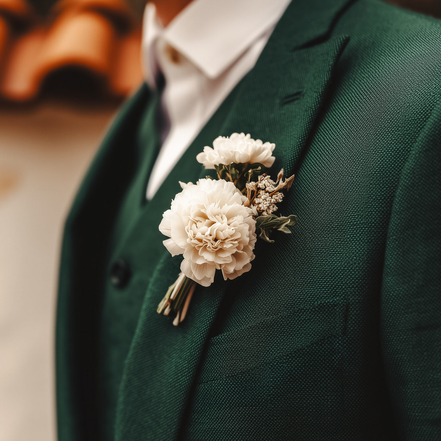 Gros plan boutonnière blanche sur veste de costume vert forêt.