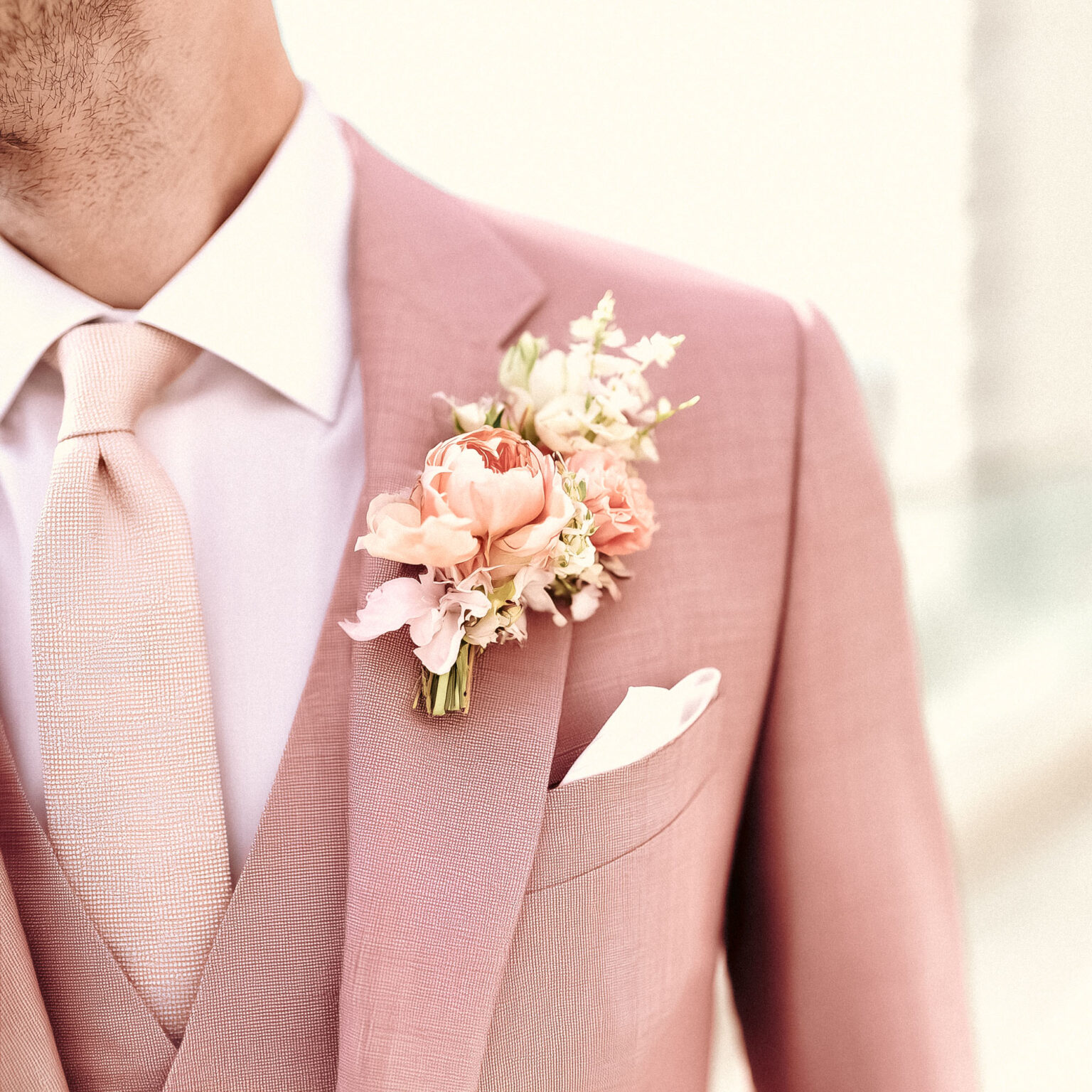 Gros plan sur boutonnière fleurie d’un costume rose poudré.