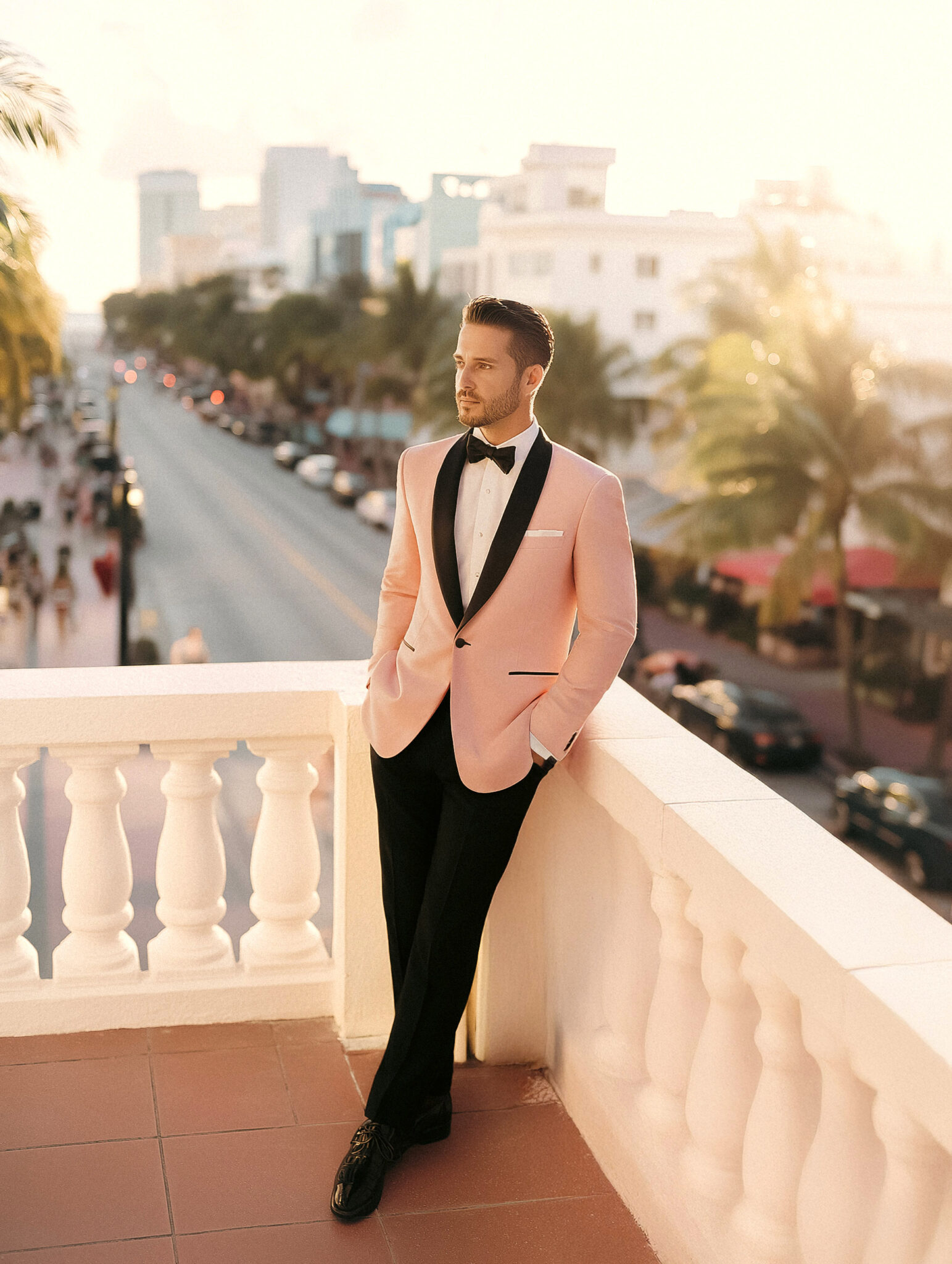 Homme en smoking rose avec pantalon noir sur terrasse d’hôtel.