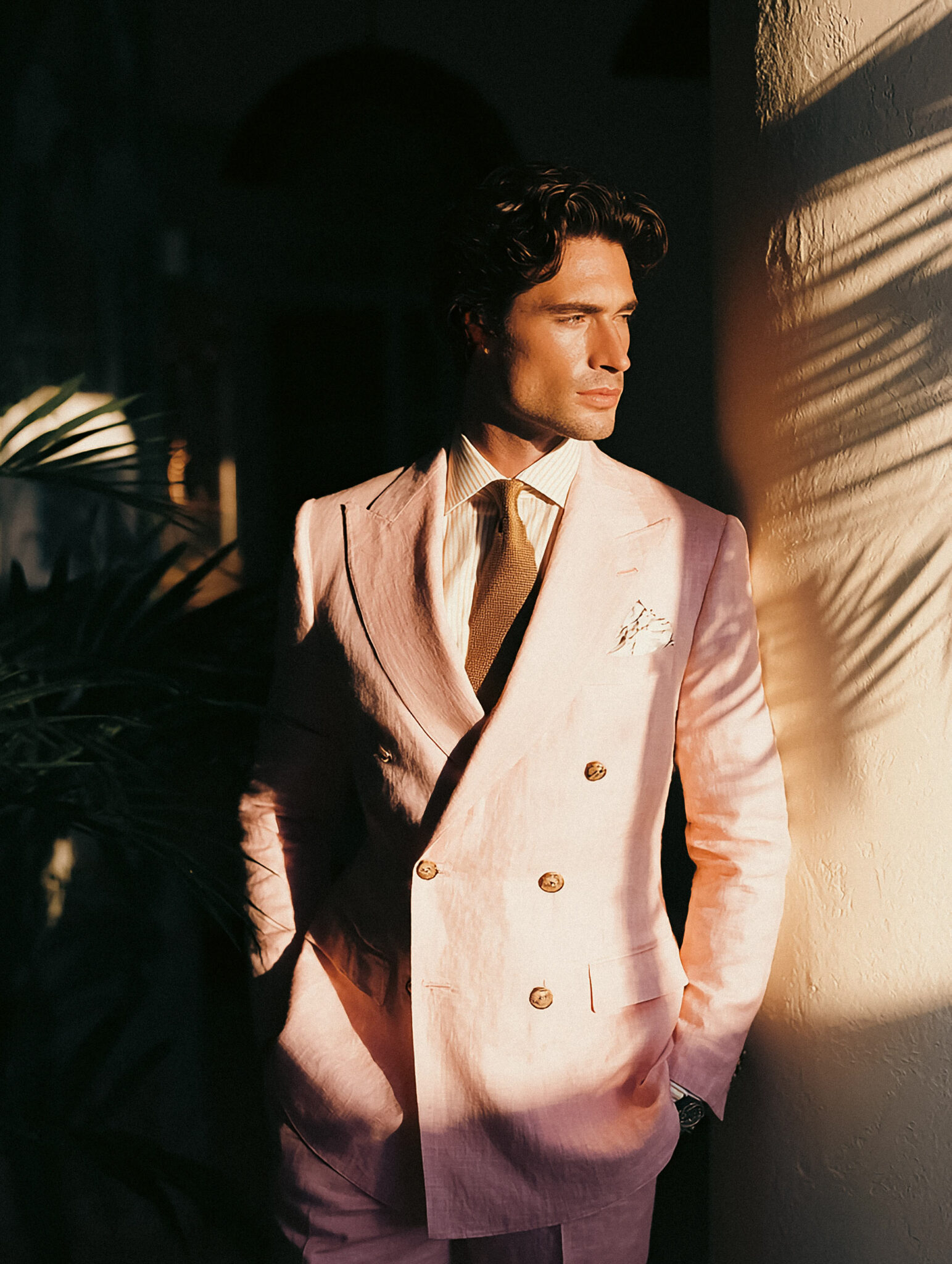 Homme en costume croisé rose lin dans la lumière du coucher de soleil.