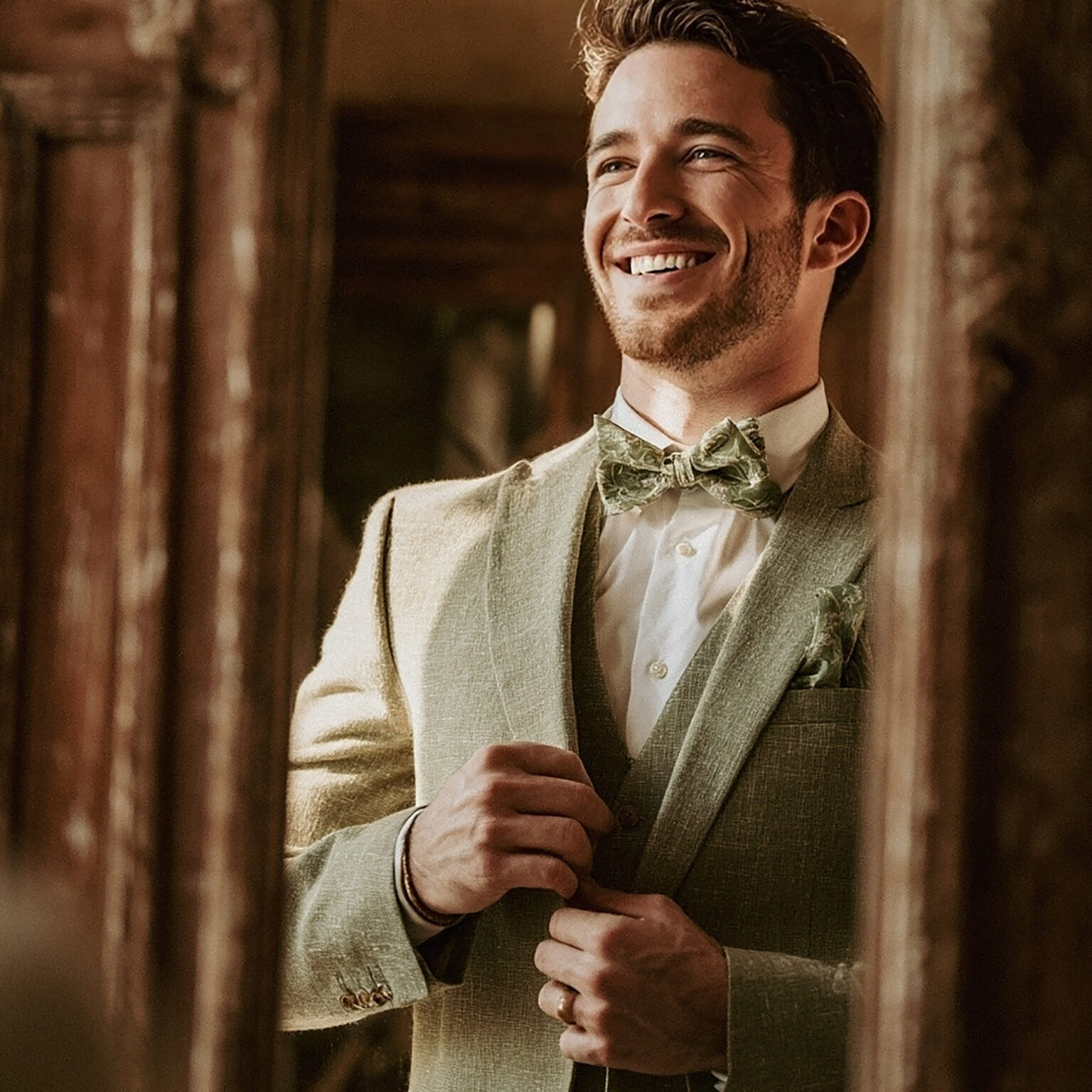Détail du marié en costume vert sauge souriant.