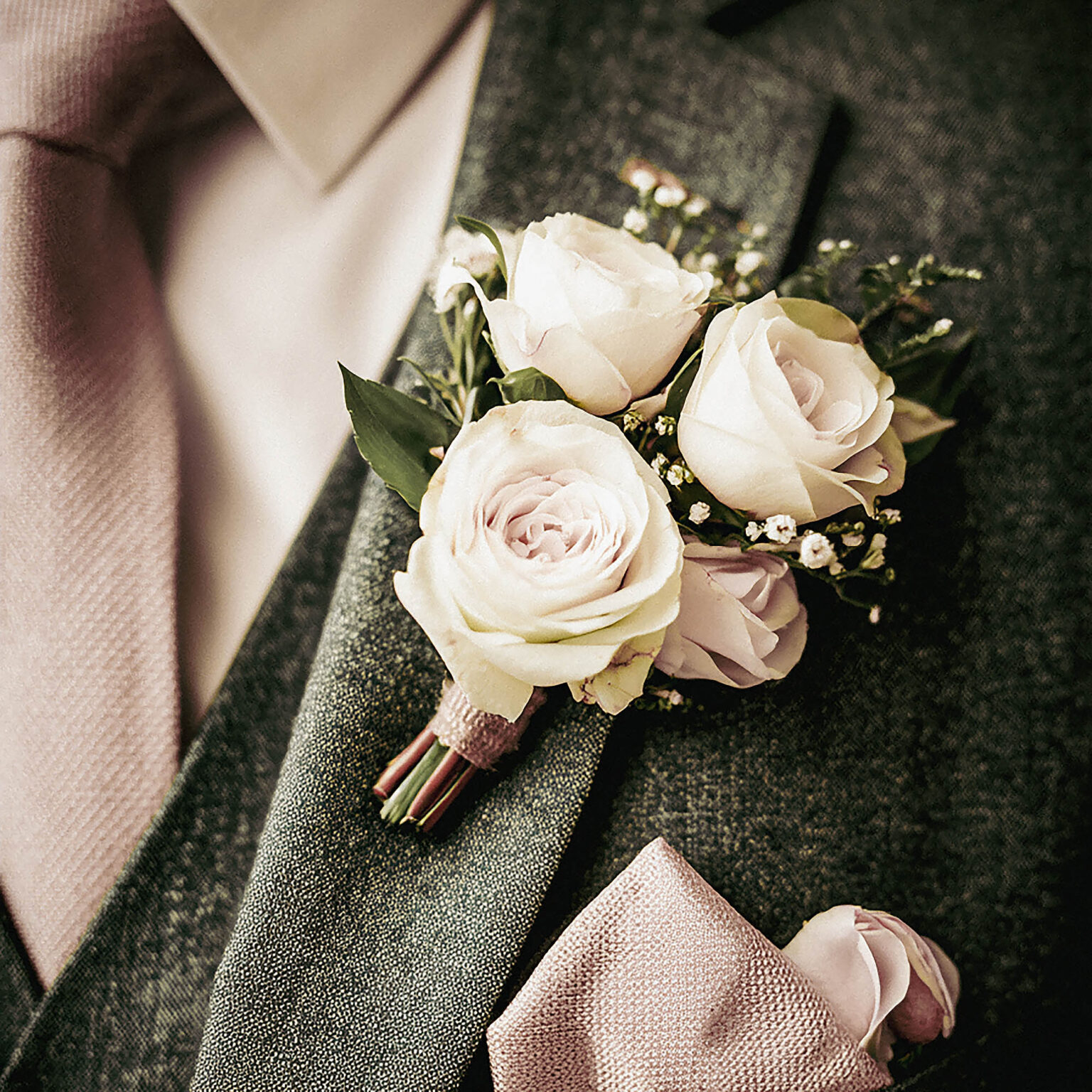 Boutonnière rouse poudré et feuillage sauge fixée sur un revers de costume vert